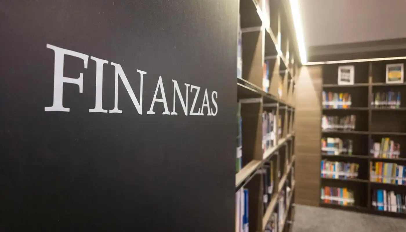 Cinco libros de finanzas personales apilados sobre una mesa de madera con luz natural