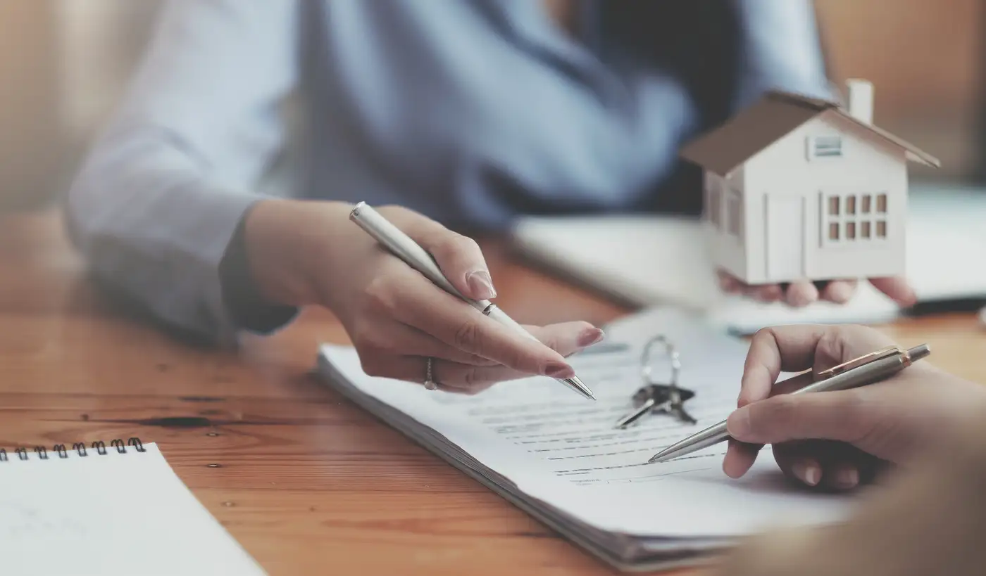 agente inmobiliario y persona firmando contrato compra de casa simbolizando hipoteca y hogar